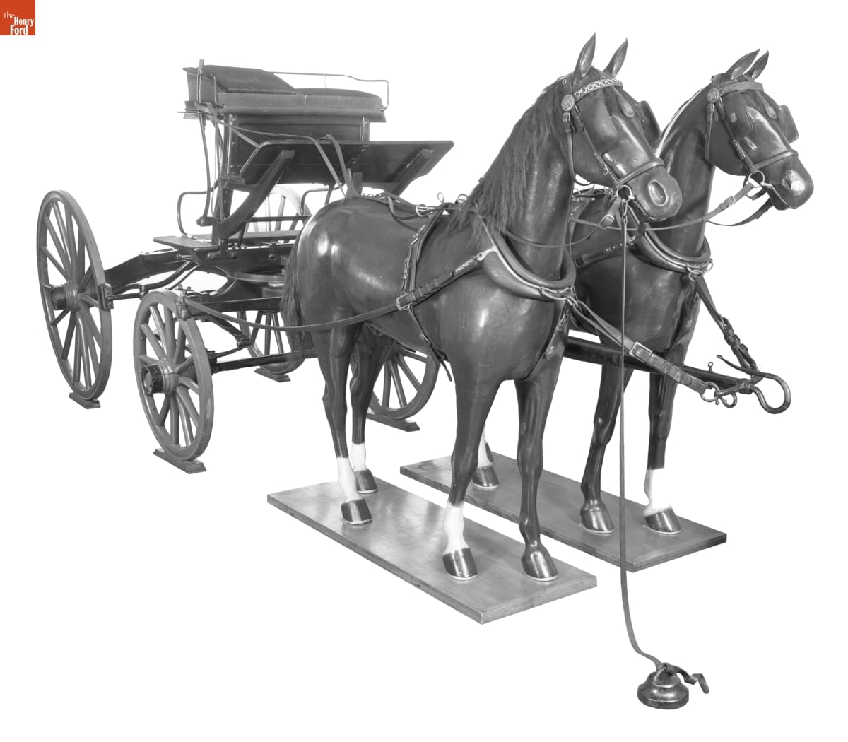 Minimal wagon with just a seat and four wheels, hitched to two horse mannequins