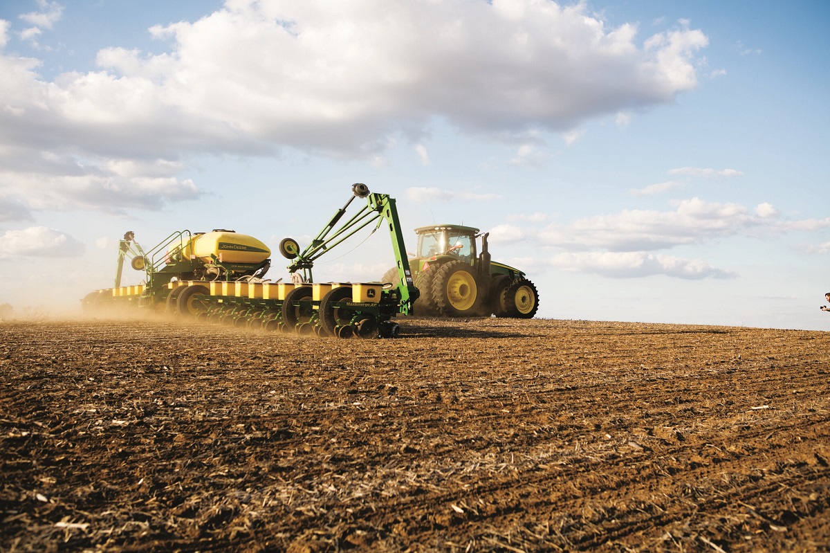 Green and yellow tractor pulls wide attachment across a dirt field