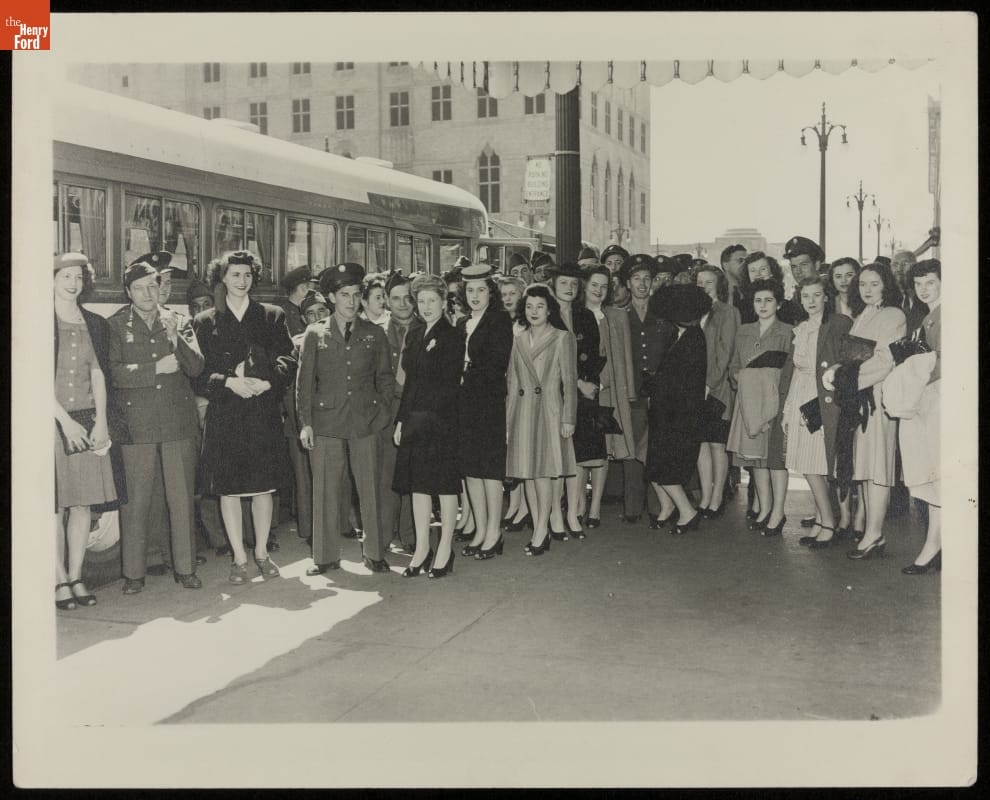 Soldiers and Hostesses Participating in an AFL-USO Event, Detroit, Michigan, 1945 Group of men in military uniforms and women in dresses stand in front of a bus, with buildings and streetlights in the background