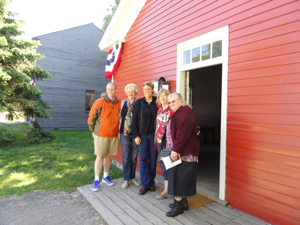 Five people with arms around each other pose for camera in front of a red wooden building