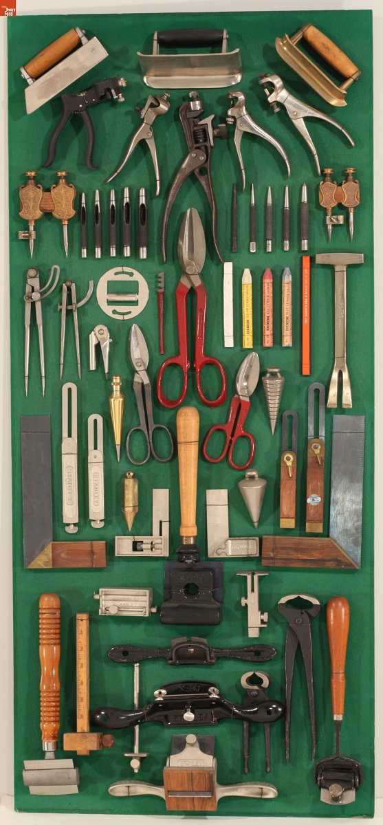 Display case containing a variety of tools hung against a green background