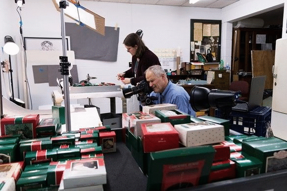 GIF cycling through two images of a man and woman with boxes of ornaments and camera 