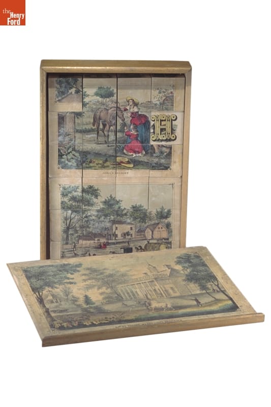 box, standing vertically with blocks with image on them in it; box lid lying in front with image on it