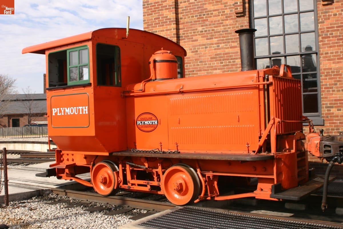 Small orange locomotive on railroad tracks by brick building