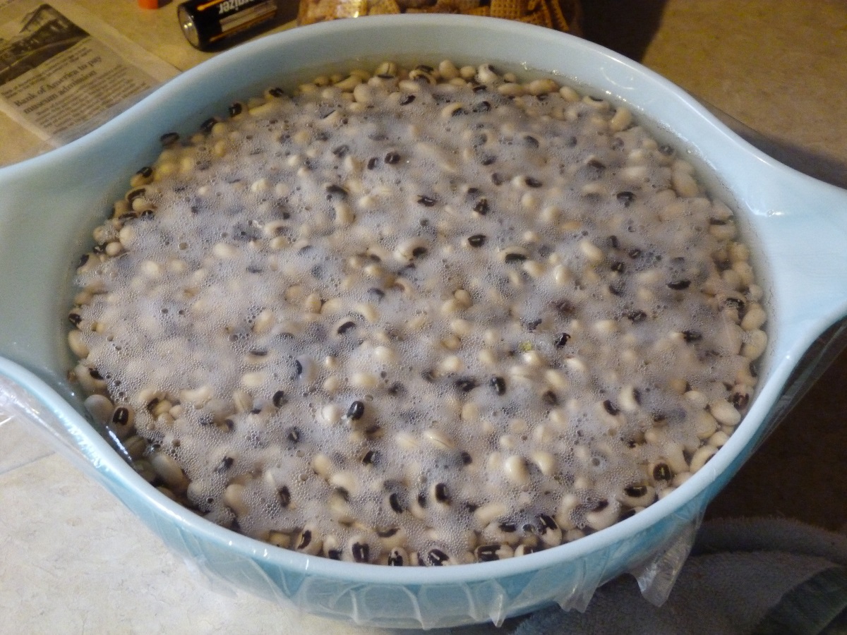 Black-eyed peas soaking in water with a bit of froth at the top in a blue-and-white bowl, covered with plastic wrap
