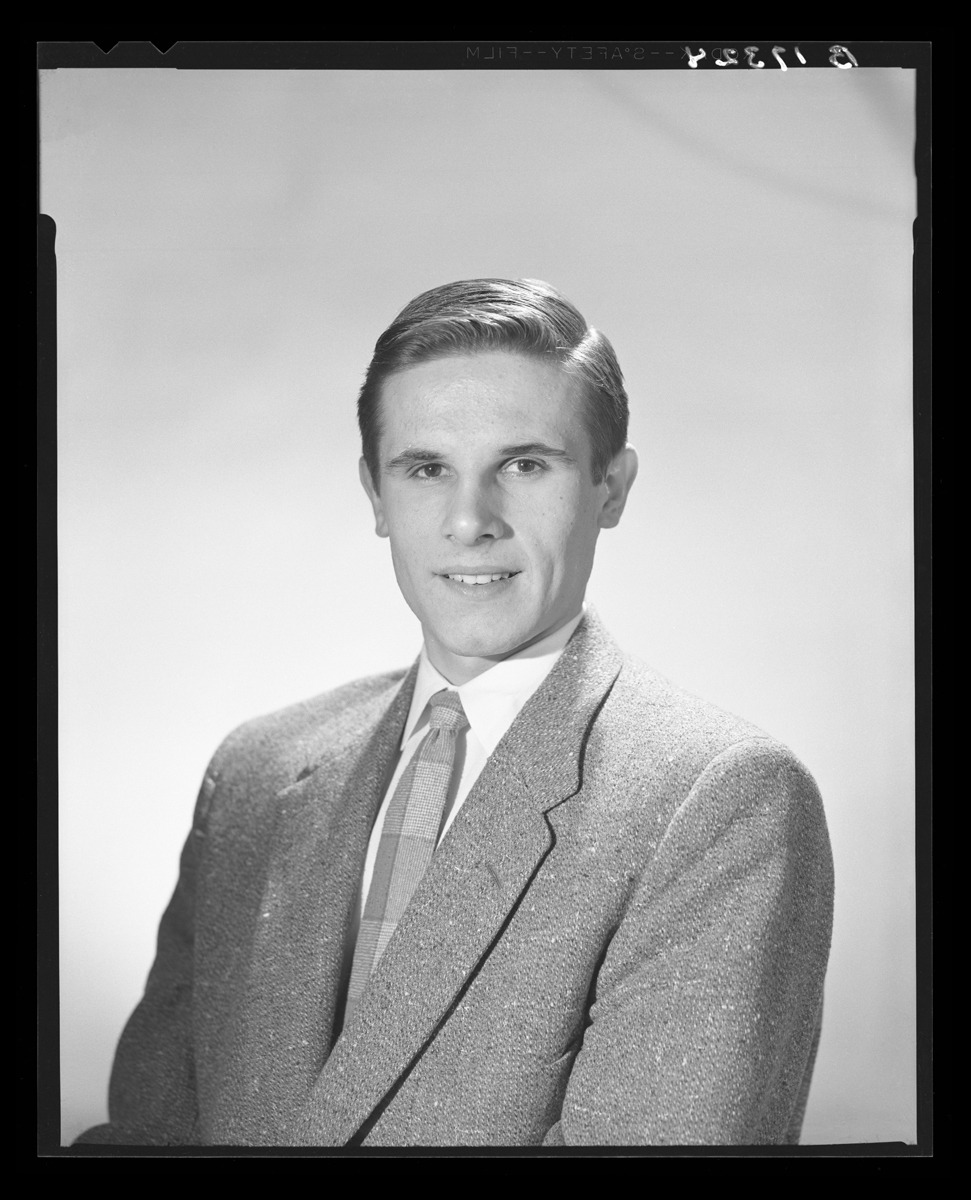 Black-and-white posed portrait photograph of young man in suit