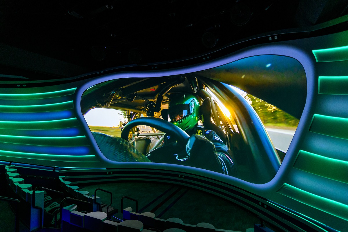 Curved theater with visor-shaped image of race car driver on screen and blue and green bars extending outward