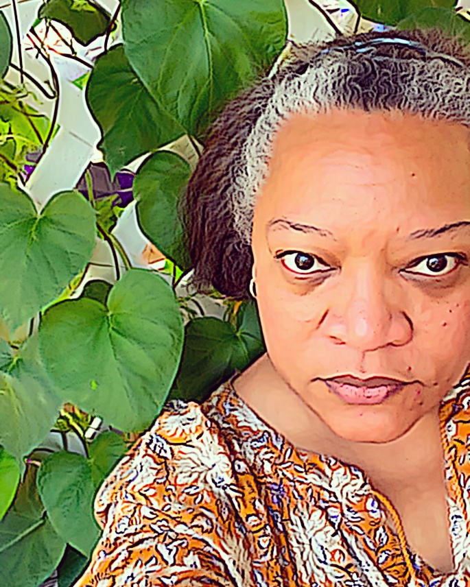 Medium-dark-skinned woman wearing print top next to a trellis with large-leafed ivy