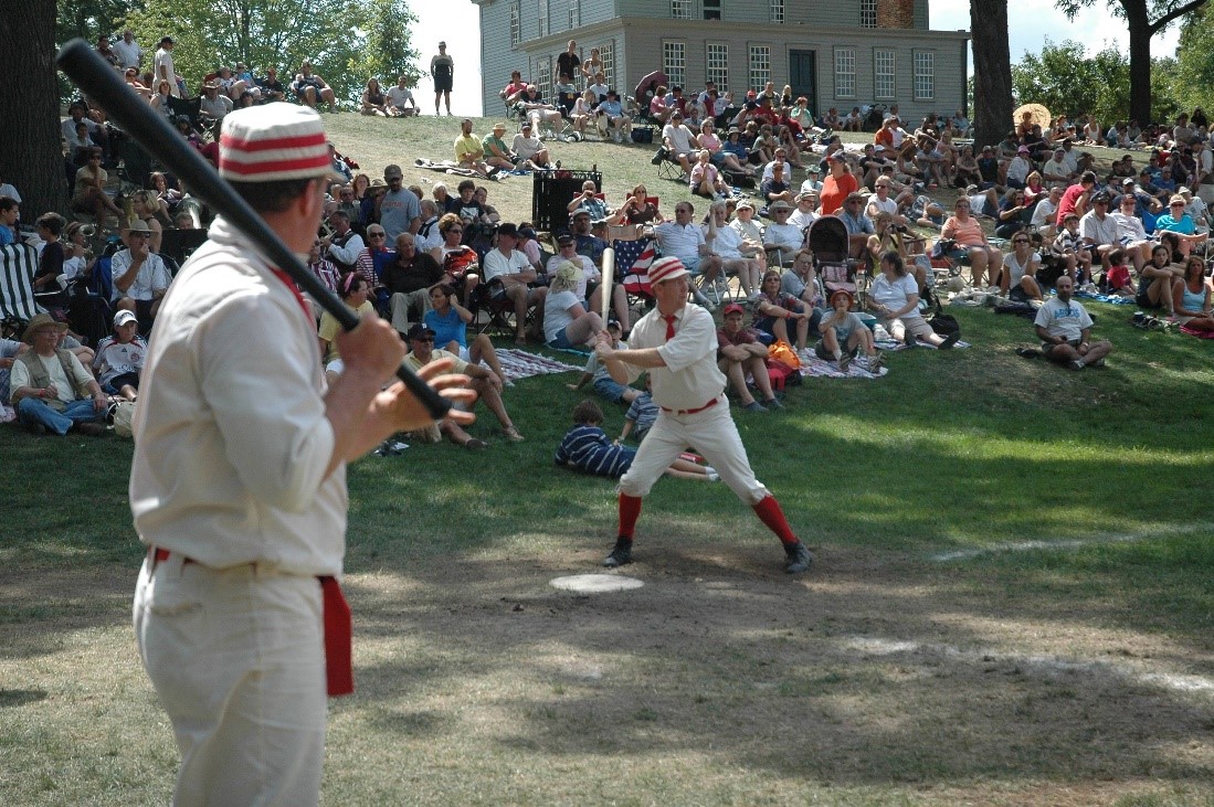 Historic Base Ball in Greenfield Village An historic base ball player holds a bat ready to swing as another stands nearby and a crowd looks on