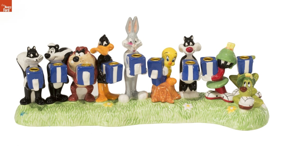 Looney Tunes Hanukkah Lamp, 1998 Nine sculpted cartoon characters, each holding a blue and white box with a hollow for a candle, on a base that looks like grass