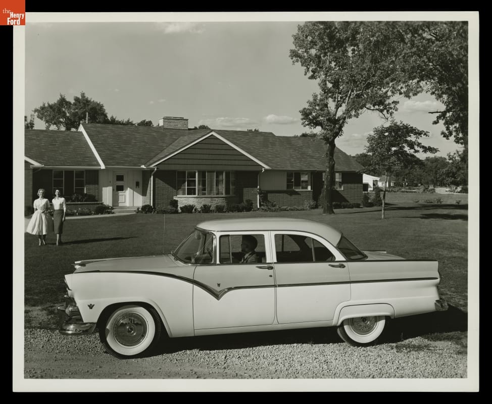 Black-and-white photo of 50s car parked in front of a lawn and house