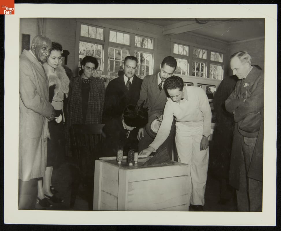 Black-and-white photo of group of people standing around a box or crate filled with concrete
