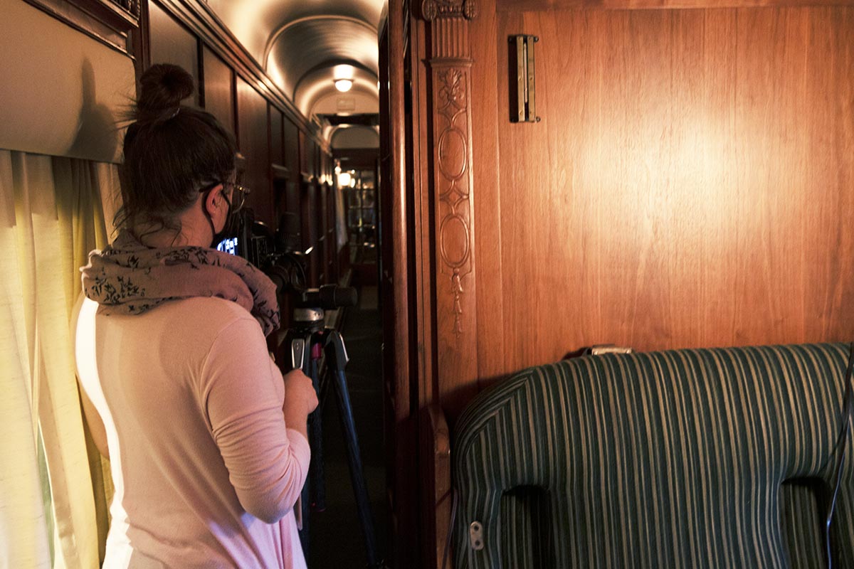 Back view of woman at camera on tripod pointing toward a narrow interior hallway