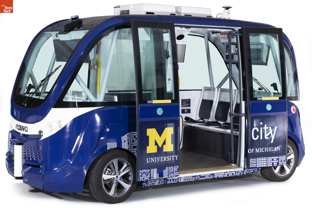 "Autonom" Driverless Shuttle Bus, Used on the University of Michigan's North Campus and Mcity Test Facility, 2017 Squat blue van with large glass windows all the way around and doors slid open; text and graphics on side