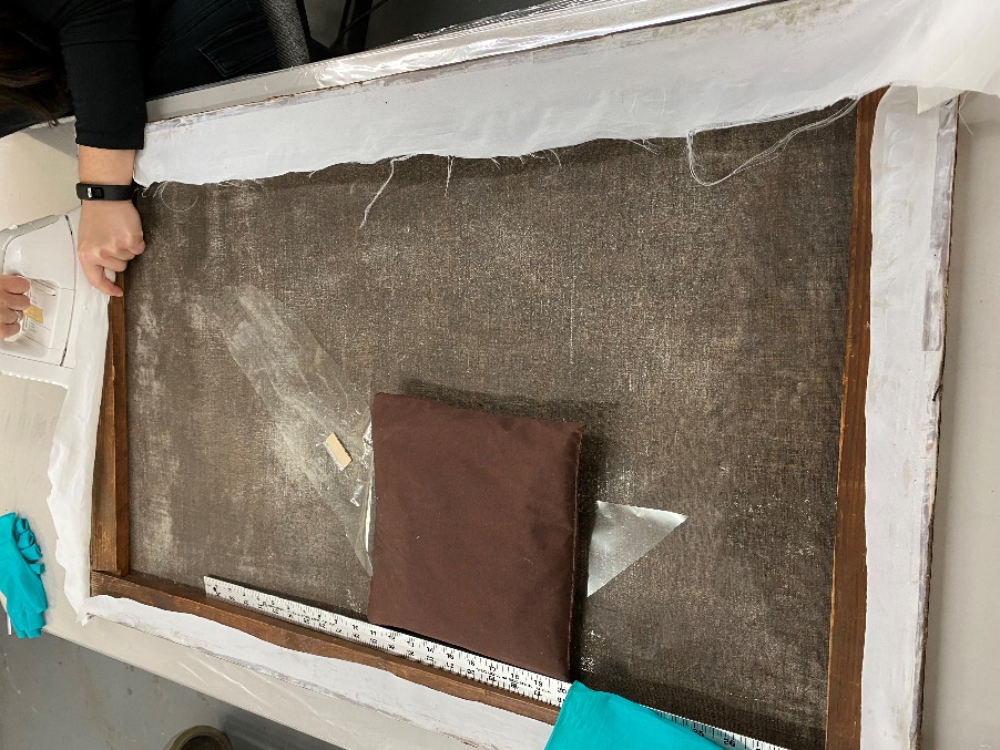 A person's hands work at top of painting laid facing down on flat table