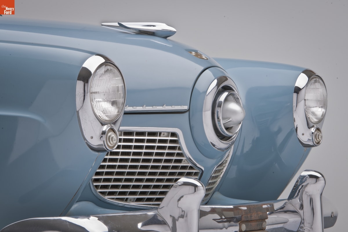 Close-up of car grille with pointed areas at either end housing headlights and in the middle