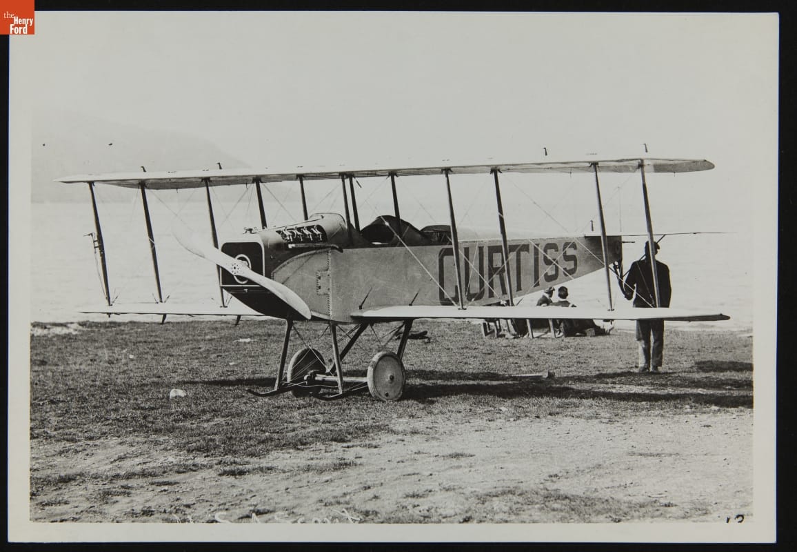 Man standing at back of airplane with large text "CURTISS" painted on side