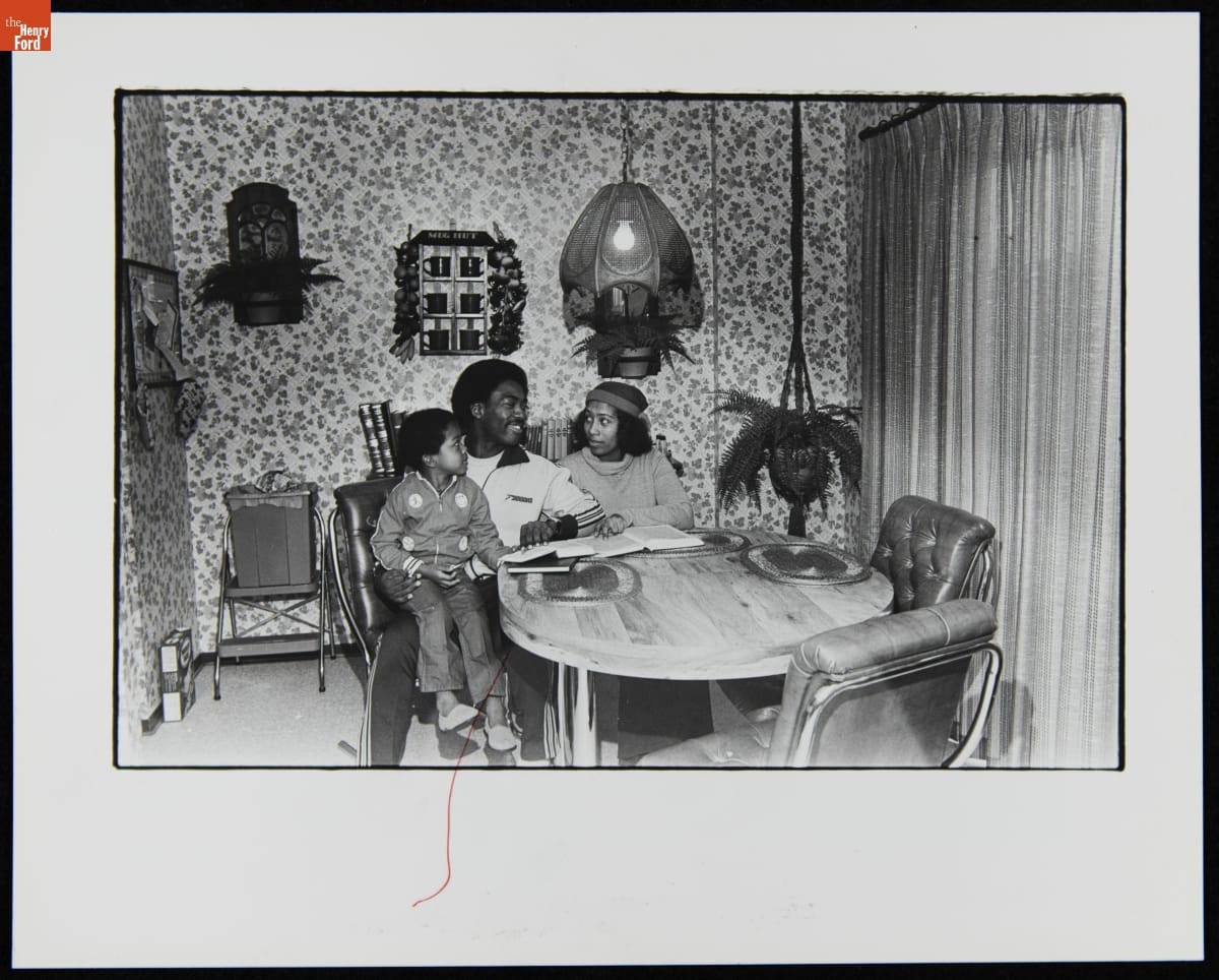 Black man, woman, and child sitting at a table with books in front of them and on a small shelf behind them
