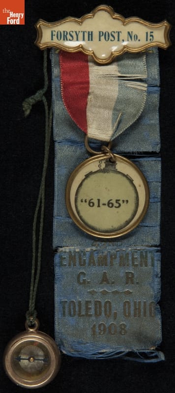 Blue ribbon containing text; topped with red, white, and blue ribbon with round metal piece containing text