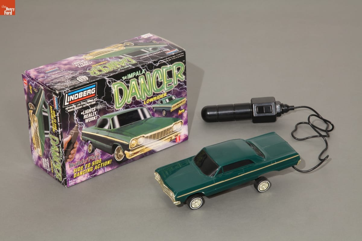 Green toy car attached to black rod-like control, along with box with text, image of same car, and black and purple pattern of lightning bolts