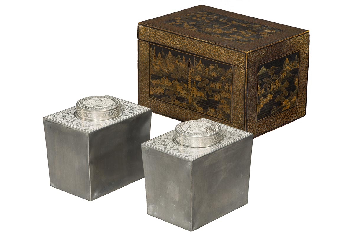Lacquered box in shades of brown and black with scene of houses and stupa; two silver cannisters with decorated tops sit in front of it