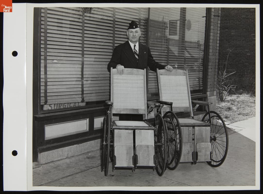 American Legion Employee with Wheelchairs Purchased for Percy Jones Veterans Hospital with Muster Out Pay, March 1944 Man in suit and military-looking cap stands with hands on two wheelchairs in front of a window with closed blinds