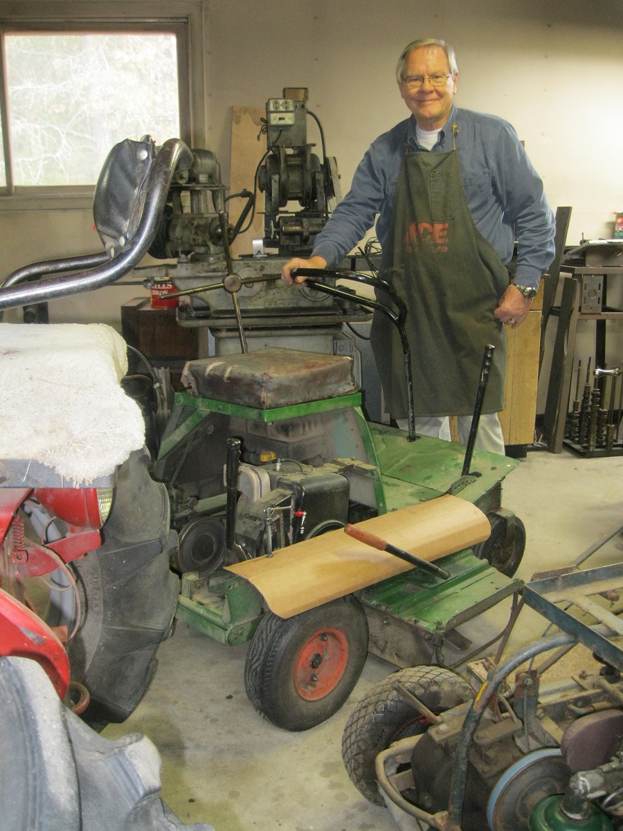 Man in denim shirt and shop apron stands in workshop next to machinery