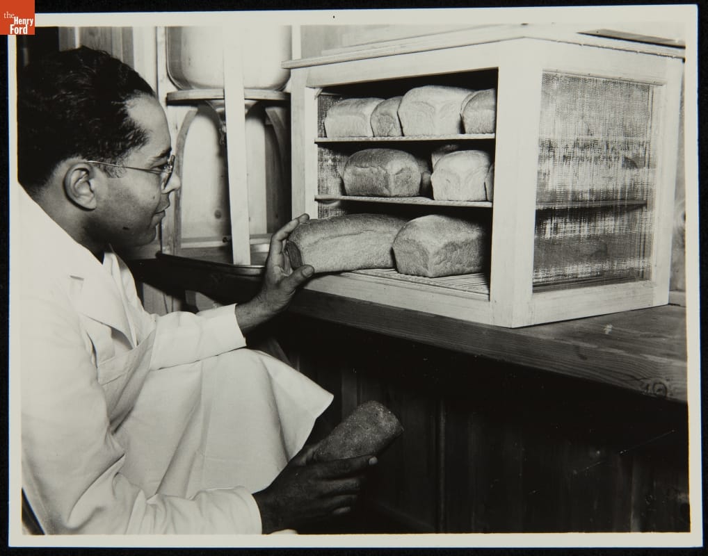 Man kneels in front of cabinet full of loaves of bread to pull a loaf out