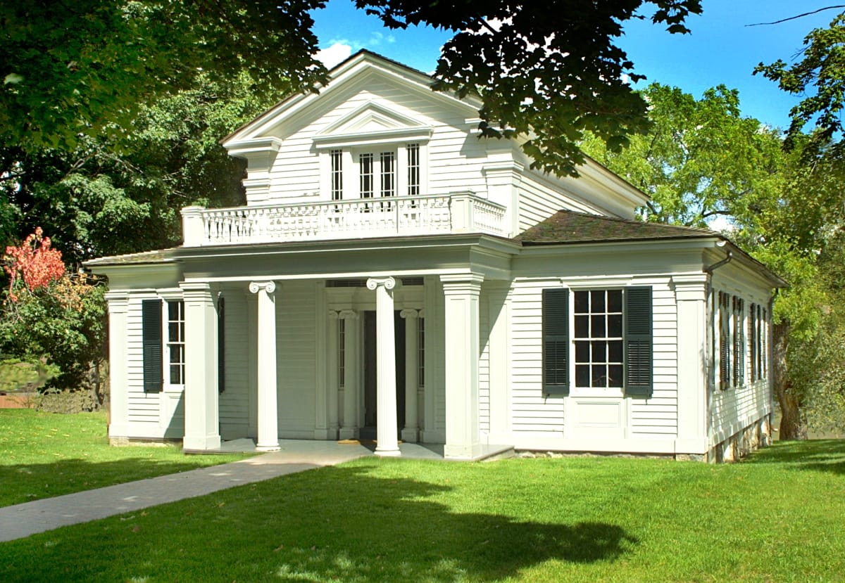 Two-story white wooden house with elaborate portico with columns, topped by a balcony