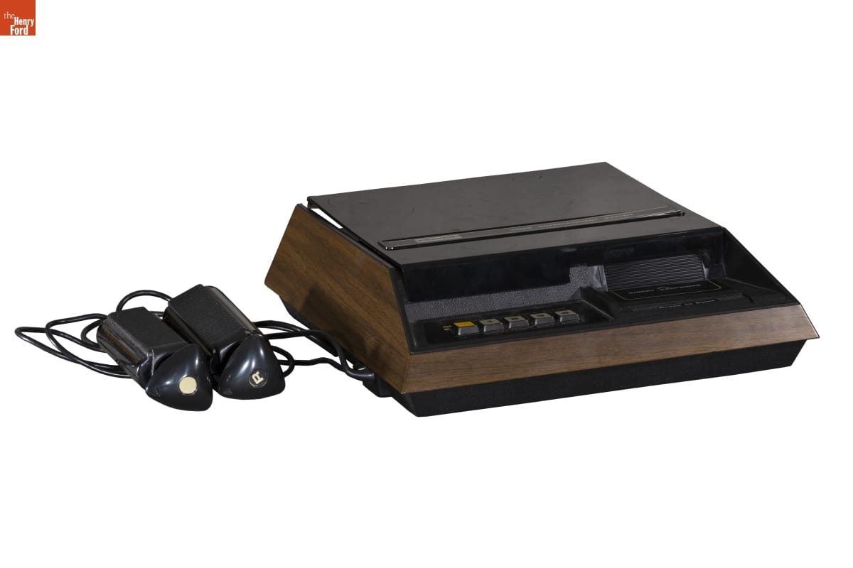 Boxy brown-and-black gaming console with two stick-shaped controllers