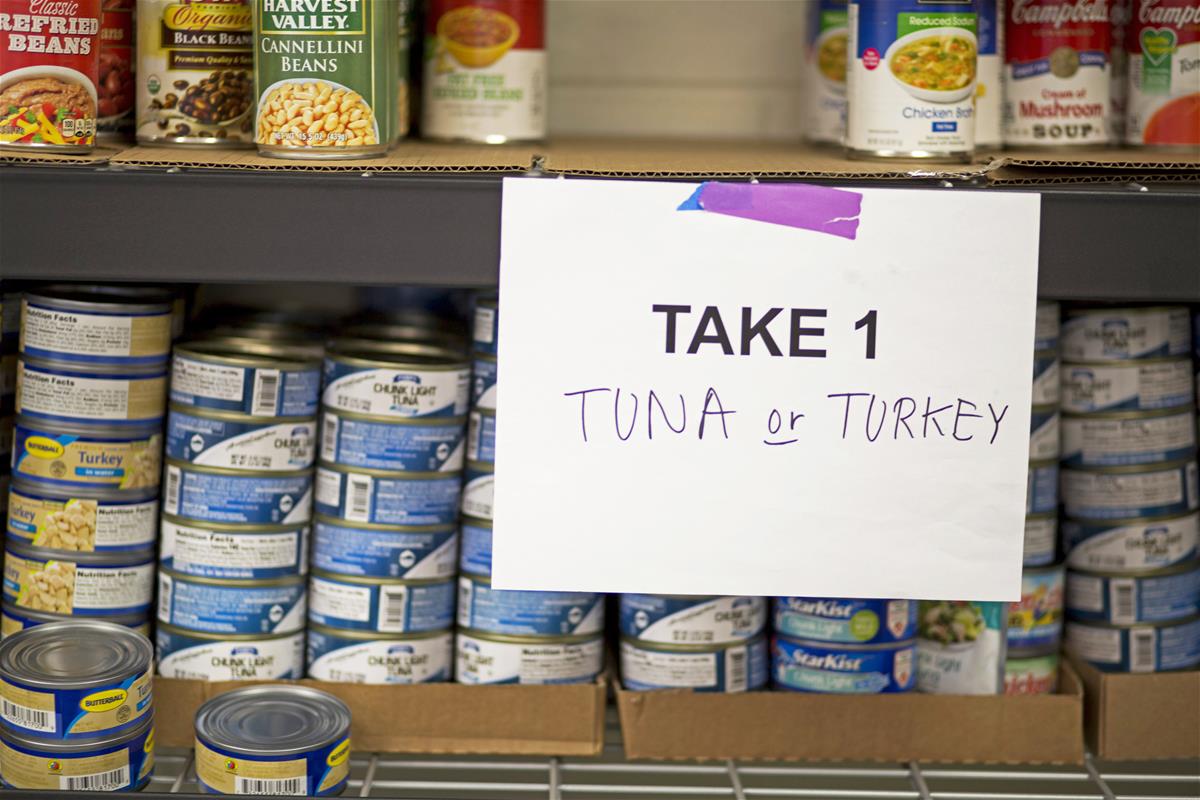 Shelves with cans of tuna, turkey, and vegetables, with sign reading "Take 1: Tuna or Turkey"