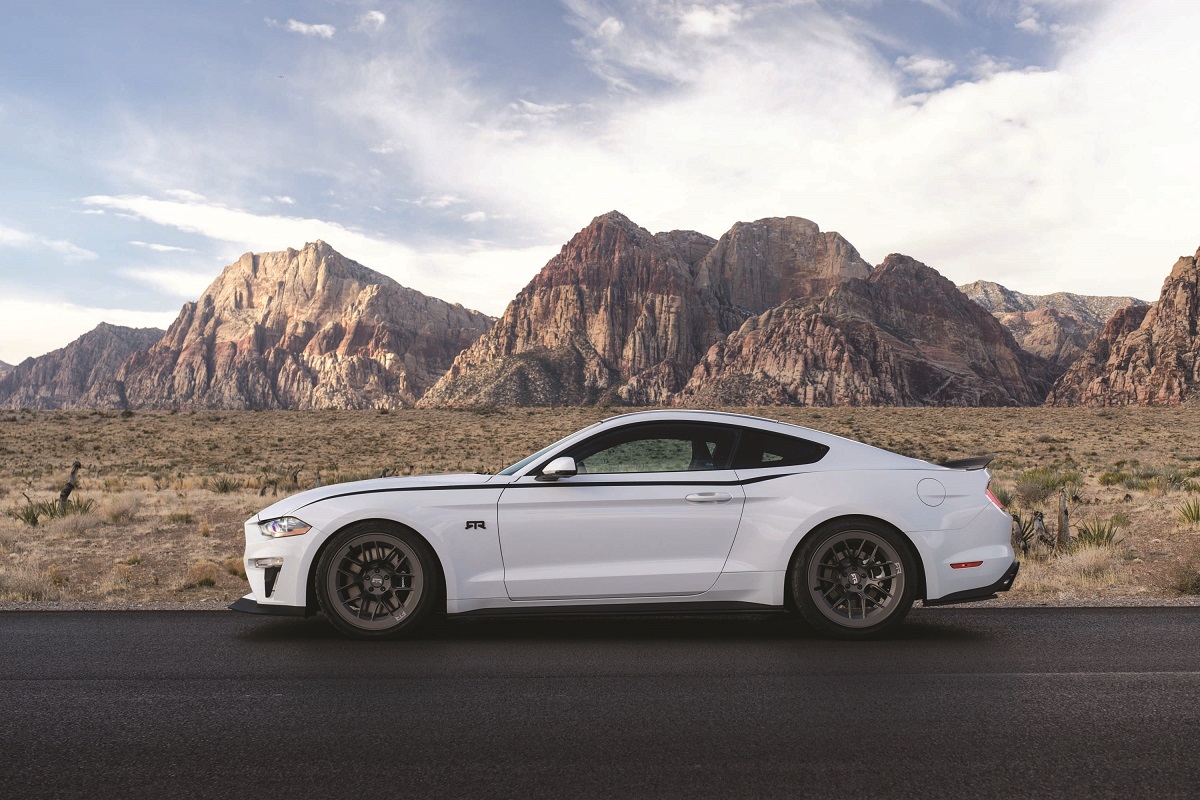 Side view of sleek white car parked on road in front of desert and mountains