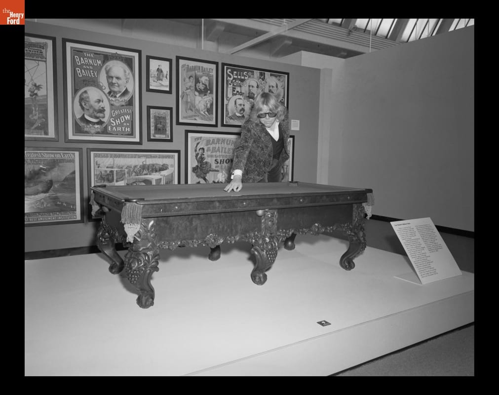 Man leans over miniature pool table in front of a wall filled with posters