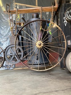 Machinery with large wheel suspended by heavy chains from a board or plank