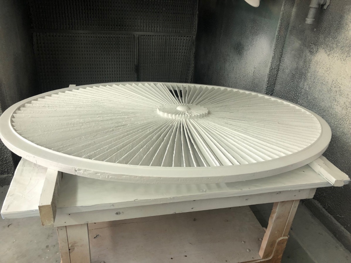 Round decorative architectural detail sitting on work table in space with paint-spattered walls 