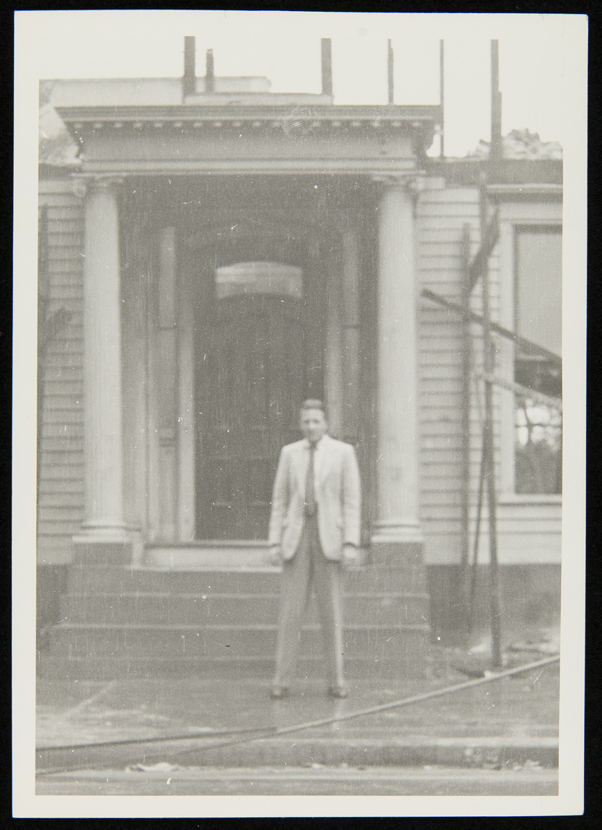 Man in suit stands in front of partially disassembled house