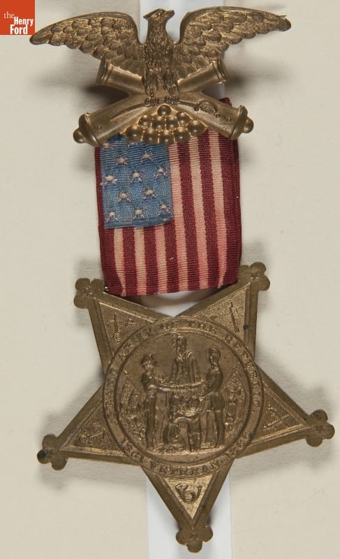 Badge with metal eagle and top and star with image and text at bottom; small U.S. flag in middle