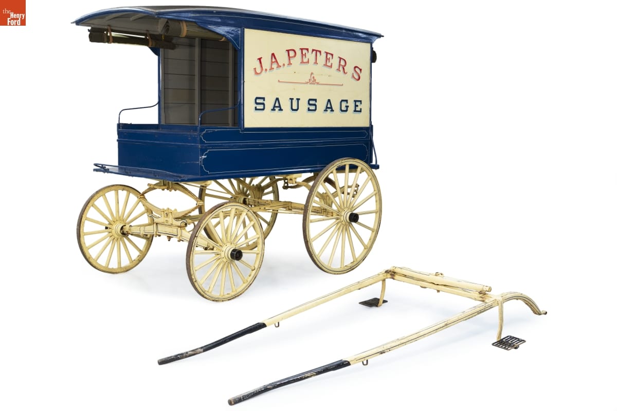 Royal blue wagon with white wheels and large white sign on side reading "J.A. Peters Sausage"
