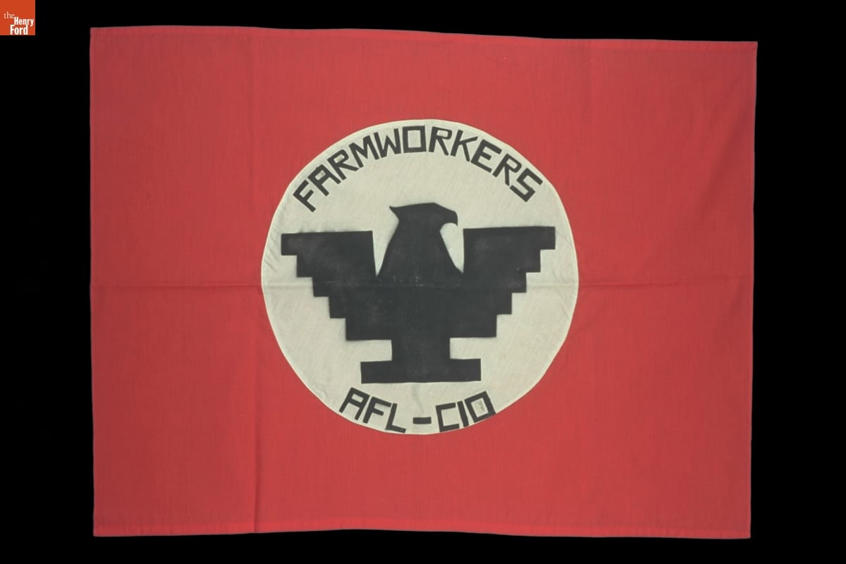 Red flag with white circle containing stylistic, blocky silhouette of eagle and text "FARMWORKERS AFL-CIO"