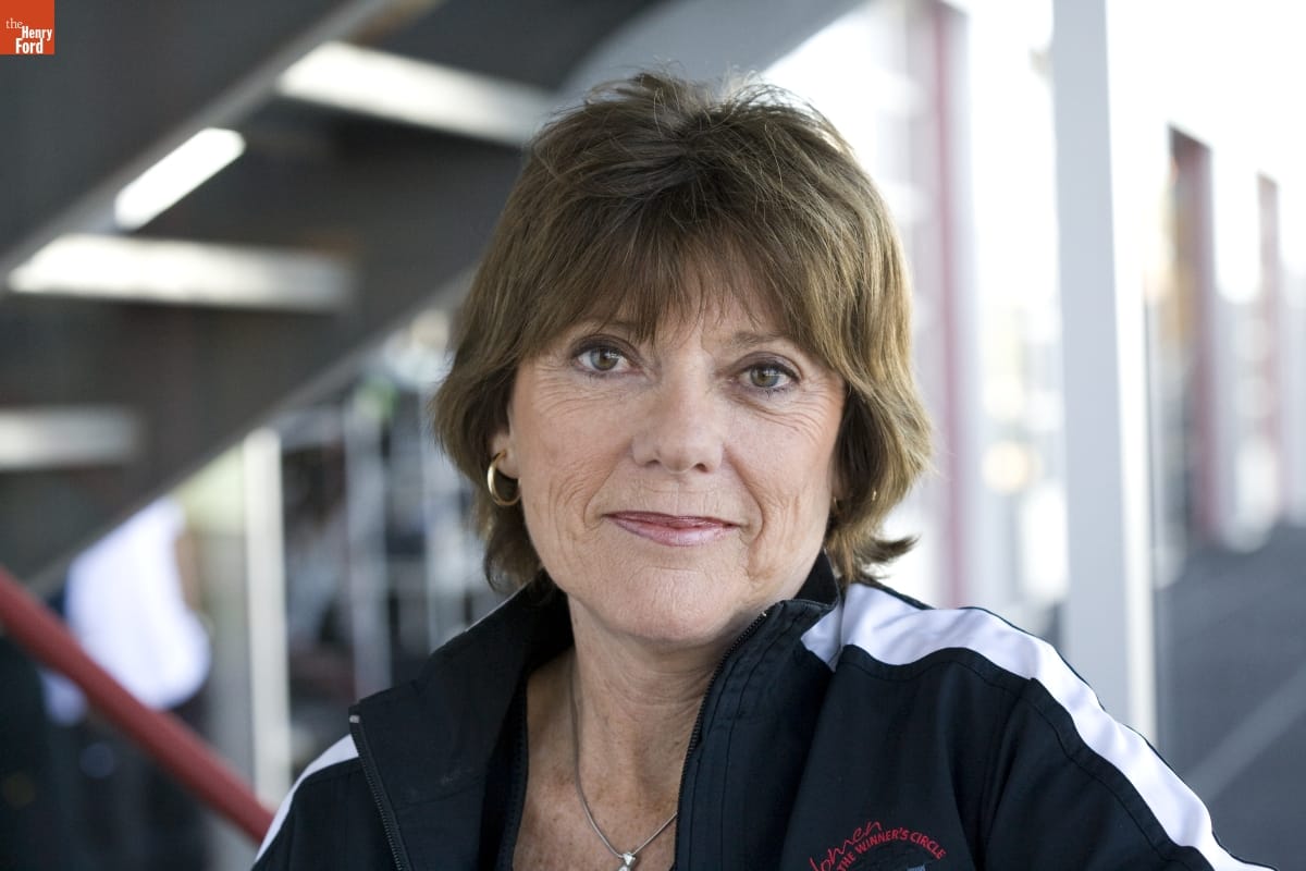 Woman with short brown hair wearing track jacket smiles toward camera