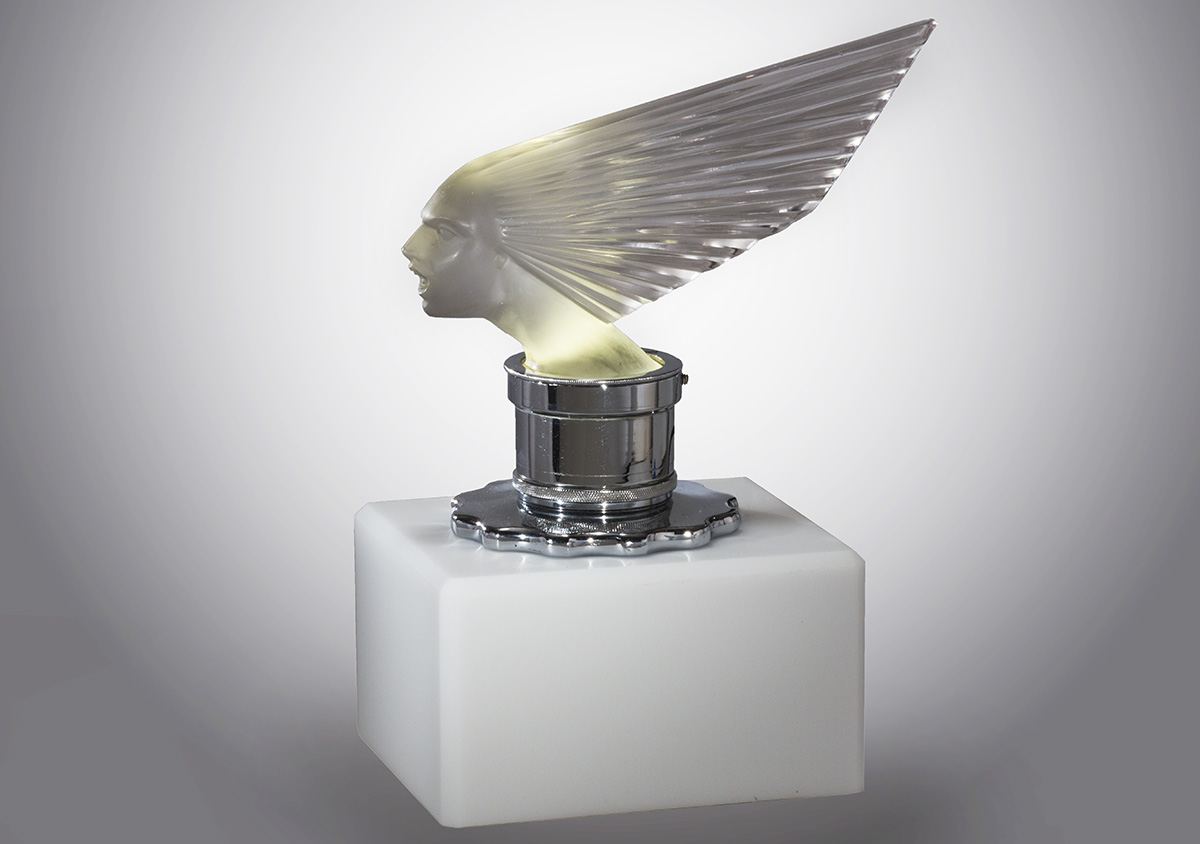 Glass sculpture of face with hair stylized into a dramatic fan backwards, atop silver base/mount