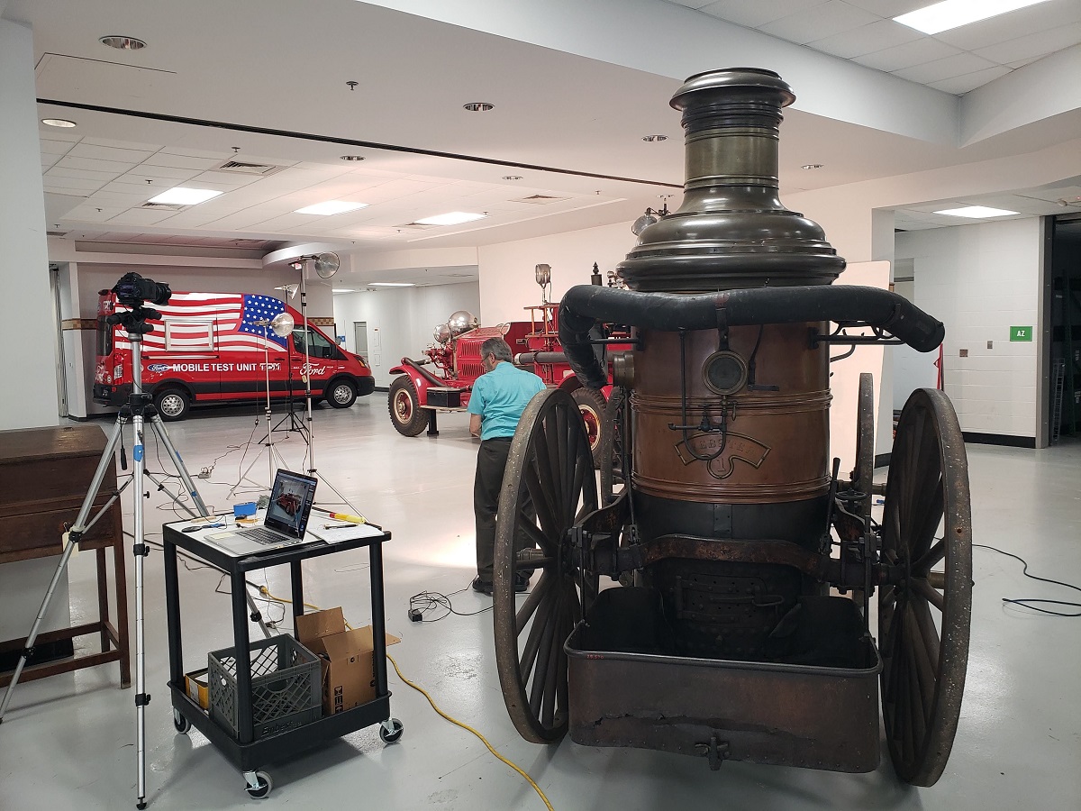 Man works at photographic equipment among several vehicles in a large room