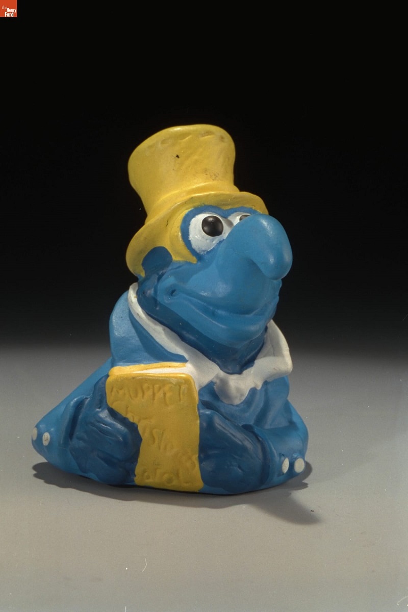 Blue creature with hooked nose, wearing yellow top hat and holding a yellow book