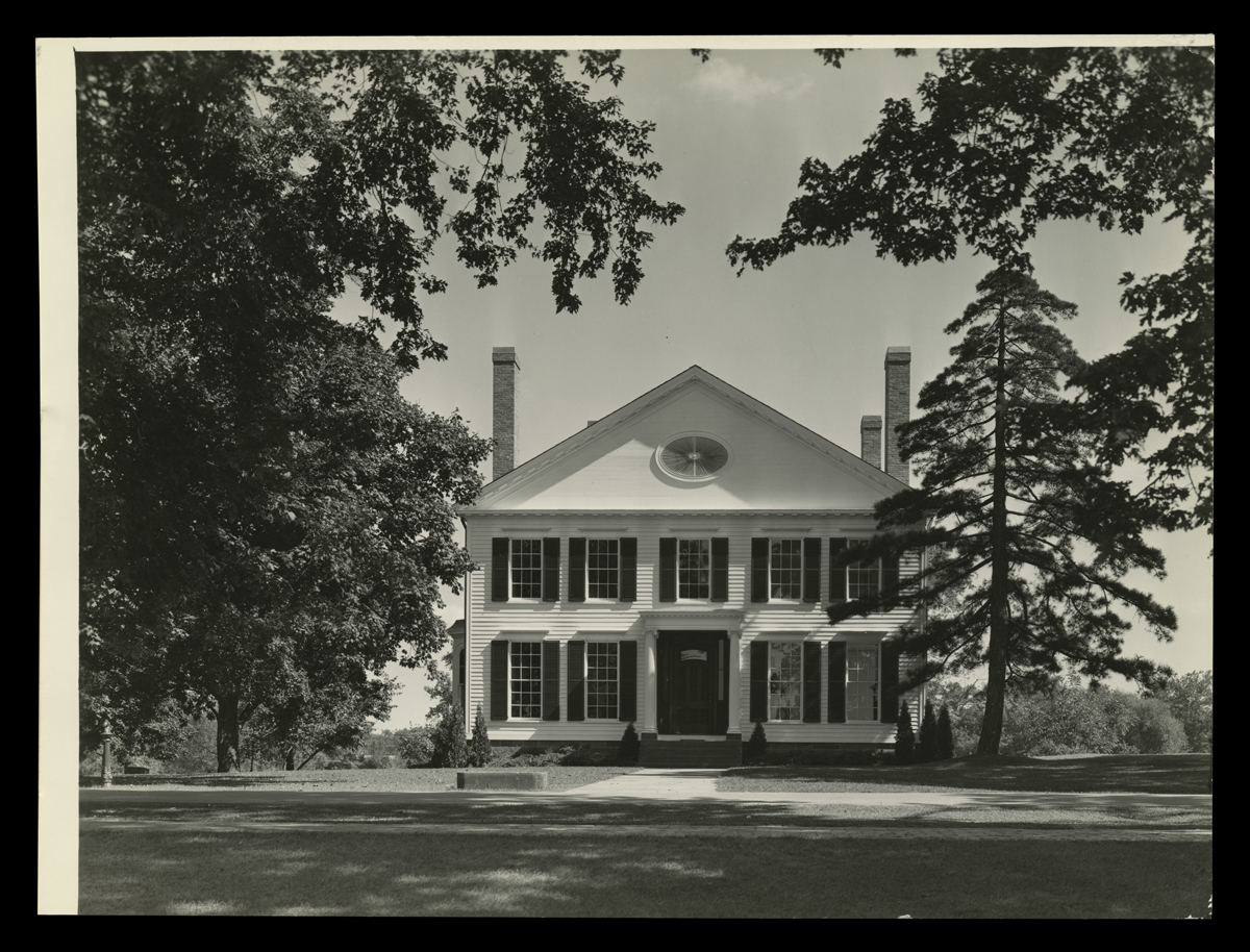 Two-story wooden house on large lawn with trees on either side