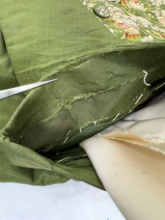 Two levels of wear are evident on the sleeves Detail of moss-green fabric with stitching and wear