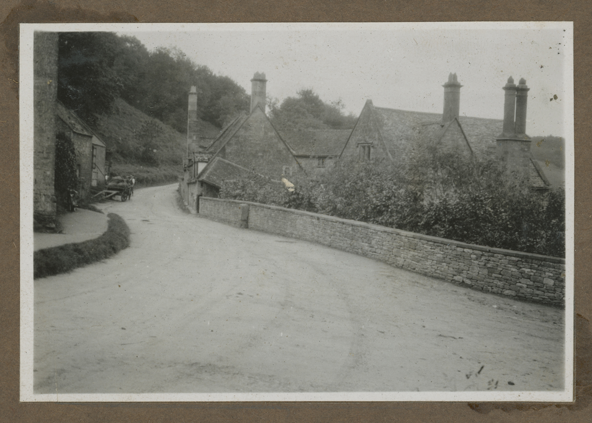 Curving dirt road with low stone buildings on either side and a wall on one side