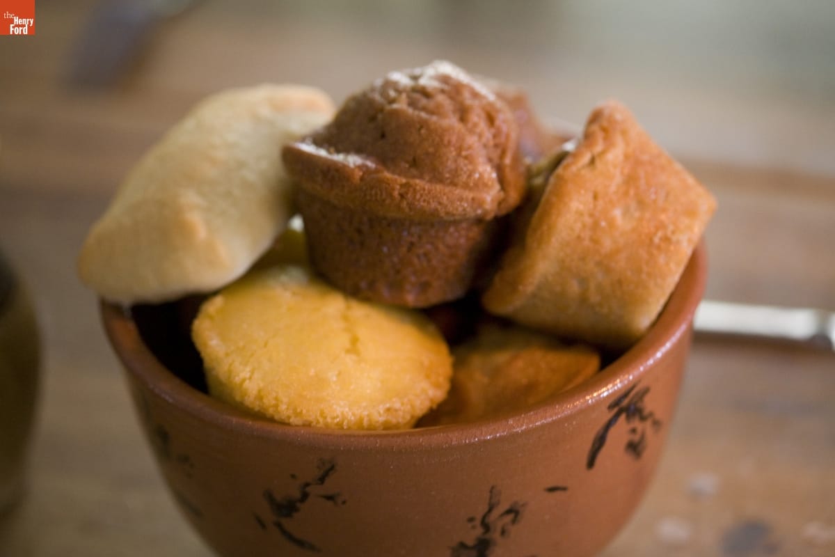 Red pottery bowl containing a variety of muffins and bread rolls