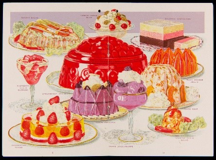 Colorful display of desserts on plates and platters and in decorative glasses; large red molded dessert in middle