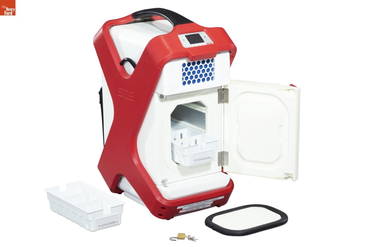 Stone Cold Systems Ice-Less Vaccine Refrigerator, 2018 White container with red "X" brace pattern and black handle; accessories pictured next to it