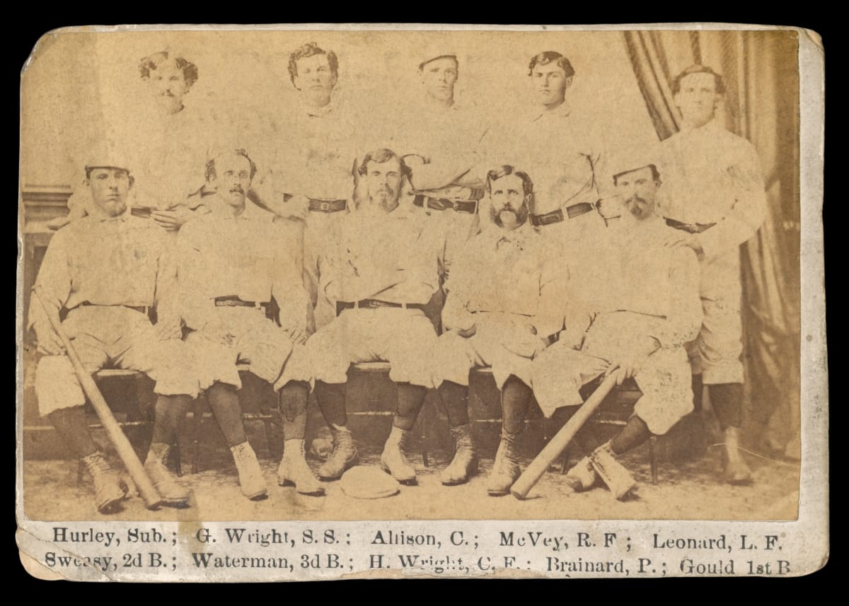 Black-and-white photo of 10 men in baseball uniforms, some holding bats, with text underneath